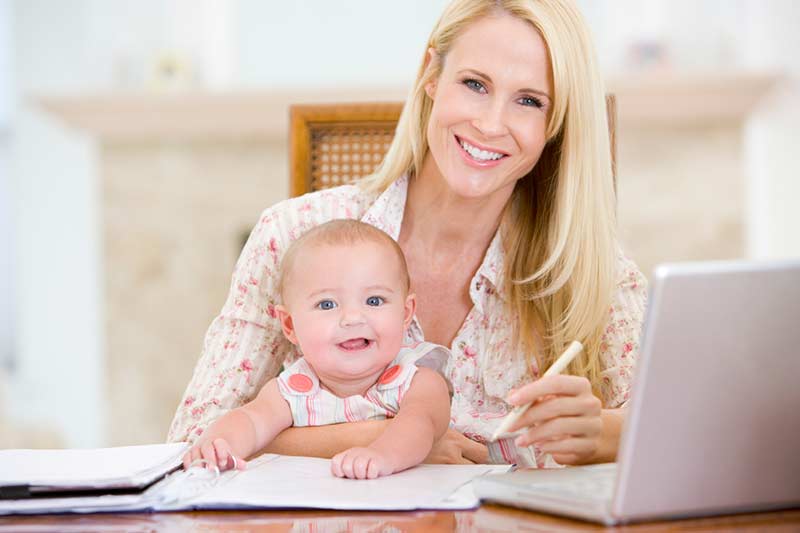 Woman holding a baby, working at a desk.